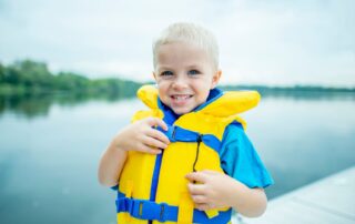 Little boy in personal floatation device by the lake. Summer safety tips for kids from Propel Physiotherapy.