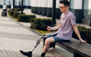 Man with prosthetic leg sitting on a bench texting. Propel Physiotherapy leg amputation rehabilitation and prosthetic fitting.