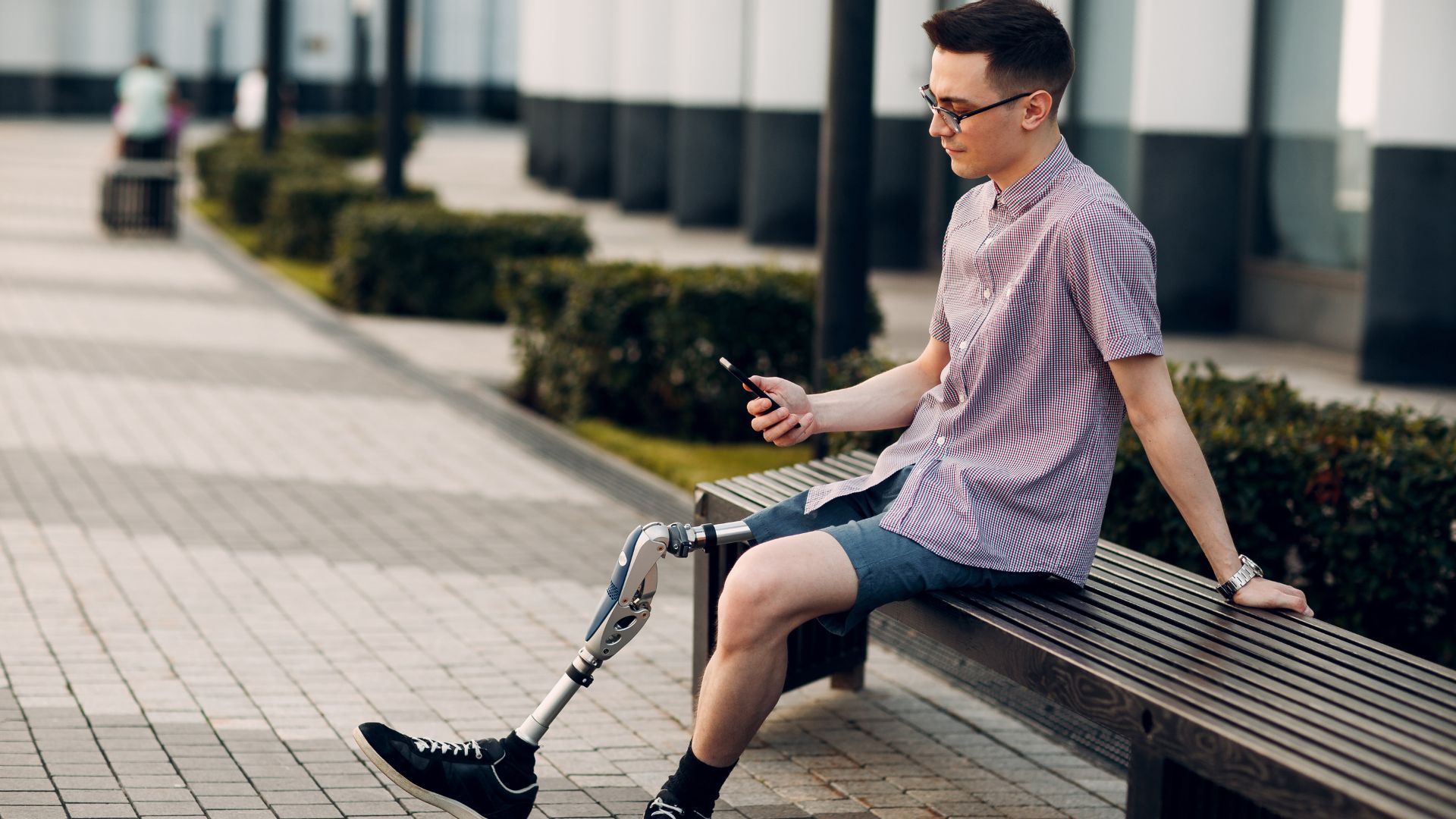 Man with prosthetic leg sitting on a bench texting. Propel Physiotherapy leg amputation rehabilitation and prosthetic fitting.