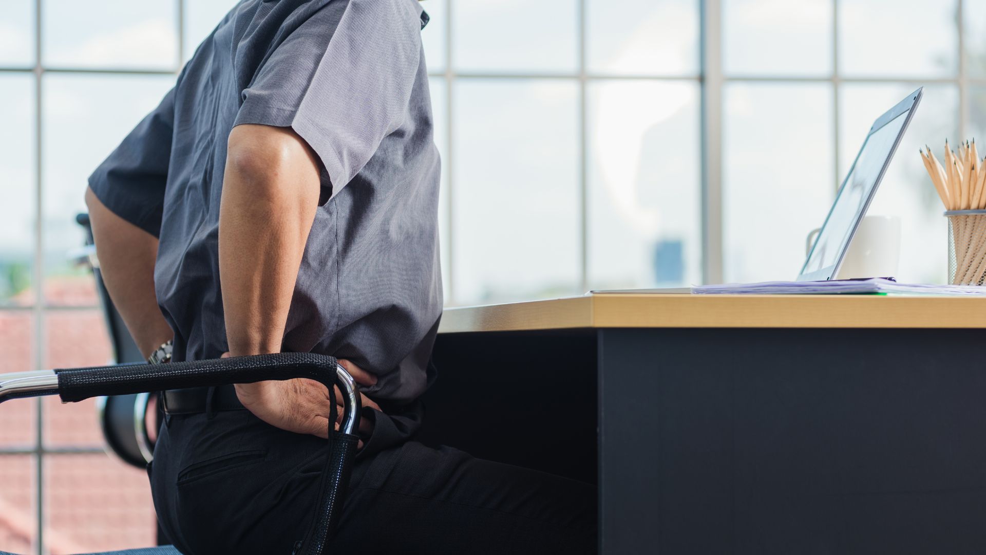 Man at desk holding sore lower back. Common office injuries causes, symptoms and treatment Propel Physiotherapy
