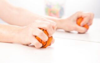 Woman squeezes ball with right hand in front of mirror box as part of mirror therapy at Propel Physiotherapy.