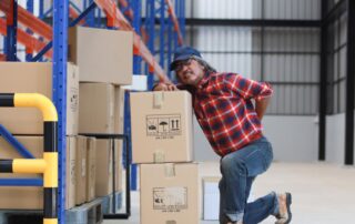 Man working in factory lifting boxes experiences back pain. Back spasm treatment at Propel Physiotherapy.