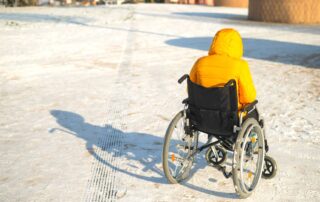 Person sitting in wheelchair outside in snowy winter weather. Wheelchair accessories and devices for winter weather. Propel Physiotherapy.