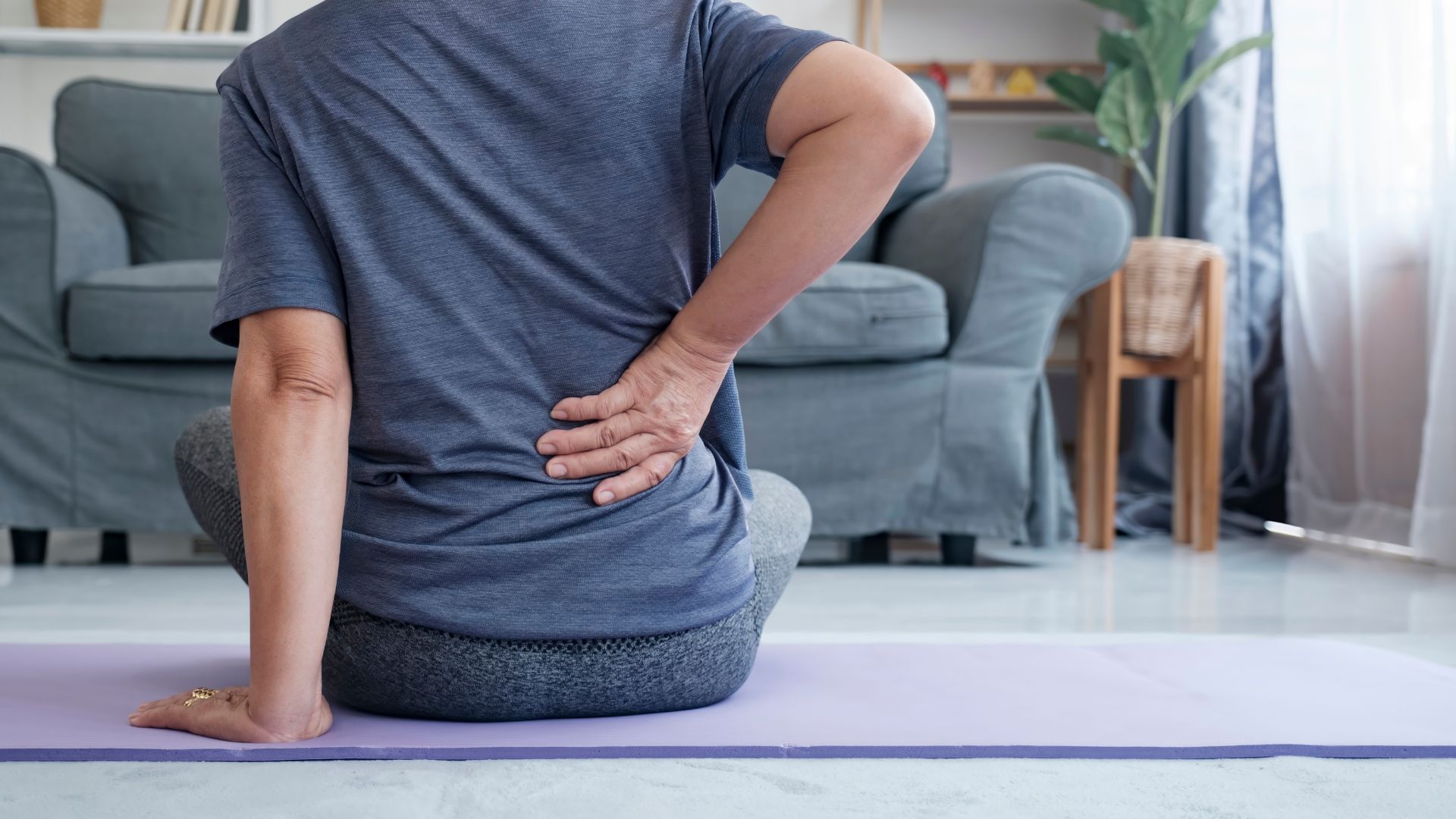 Woman sitting on the floor holding low back. Pelvic floor dysfunction and low back pain connection. Pelvic floor physiotherapy at Propel Physiotherapy.