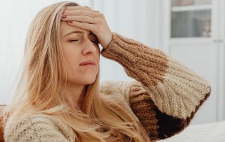 Young woman sits with hand on her forehead and look of pain on her face. Occupational therapy concussion treatment Propel Physiotherapy.