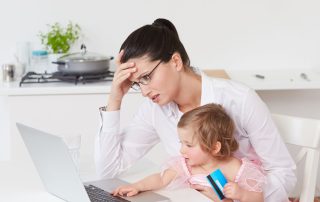 Woman working on laptop with baby on her lap and pot on the stove. Stress and how it affects the body. Propel Physiotherapy