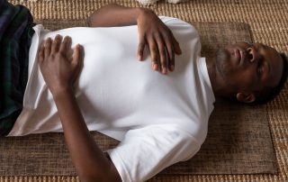 Man lying on a mat on the floor with one hand on his chest and another on his stomach doing breathing exercises. Treatment of cardiovascular effects from long COVID. Propel Physiotherapy.
