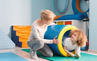 Child crawling through play tub at indoor play centre with therapist facilitating. Why physical activity matters for kids with autism. Propel Physiotherapy.