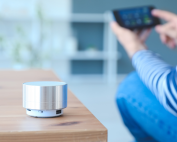 Women sitting next to a coffee table with a smart home assistant sitting on it while holding her cell phone. Smart home technology to support aging in place. Propel Physiotherapy's healthy aging solutions.