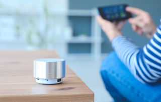 Women sitting next to a coffee table with a smart home assistant sitting on it while holding her cell phone. Smart home technology to support aging in place. Propel Physiotherapy's healthy aging solutions.