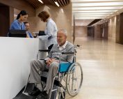 Patient in wheelchair being discharged from hospital. Spouse signing forms at the registration desk. Propel Physiotherapy hospital discharge planning questions.