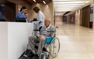 Patient in wheelchair being discharged from hospital. Spouse signing forms at the registration desk. Propel Physiotherapy hospital discharge planning questions.
