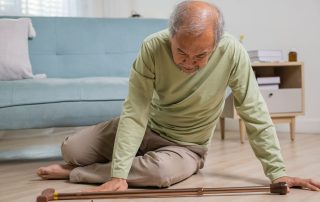 Elderly man with cane on the floor next to his couch after a fall in the living room of his home. Safe techniques for how to get up from the floor after a fall. Propel Physiotherapy.