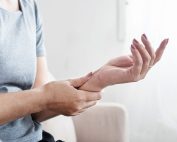 Middle-age female sitting on the couch at home holding her left forearm with her right hand with left hand palm facing up. She is experiencing menopause joint and muscle pain, carpal tunnel. Propel Physiotherapy can effectively help manage menopause joint and muscle pain and other MSK symptoms by focusing on exercises that strengthen muscles, improve flexibility, and enhance joint mobility, as well as providing education, manual therapy and other modalities that aid in pain management.