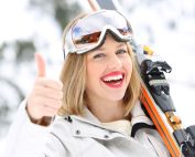 Young woman holding skiis over her left shoulder with ski goggles on her head gives the thumbs up while smiling. Skier's thumb treatment with hand therapist Ana Gollega at Propel Physiotherapy.