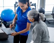 Female physiotherapist holding a clipboard and pen shows it to a seated, mature female client while talking to her about her treatment plan. Tips for choosing the right physiotherapist.