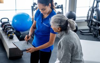Female physiotherapist holding a clipboard and pen shows it to a seated, mature female client while talking to her about her treatment plan. Tips for choosing the right physiotherapist.