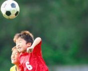 Two young children playing soccer jumping up to head the ball and colliding with each other. Soccer concussion symptoms, treatment and prevention at Propel Physiotherapy.