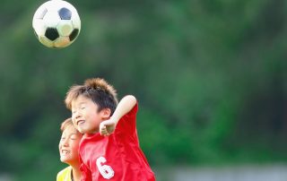 Two young children playing soccer jumping up to head the ball and colliding with each other. Soccer concussion symptoms, treatment and prevention at Propel Physiotherapy.