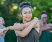 Group of people in a park holding their left arm across the front of the chest with the right arm to stretch their left shoulder. Types of Stretching: Static, Dynamic, Ballistic and PNF Stretching Explained by Kathy Mileski at Propel Physiotherapy.