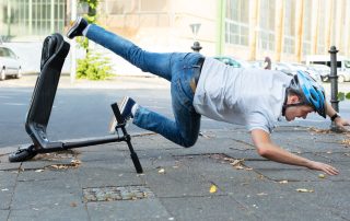 Young man wearing helmet falling off e-scooter onto stone walkway. E-scooter injury prevention tips from Propel Physiotherapy.